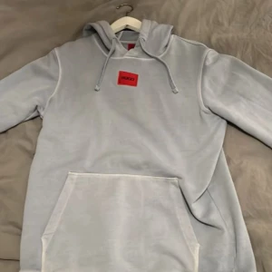 Blå hoodie från Hugo boss - Säljer en snygg och bekväm grå hoodie från Hugo. Den har en klassisk känguruficka och justerbar huva med dragsko. Perfekt för en avslappnad stil och passar till alla tillfällen. Den är i bra skick och redo för en ny ägare! 