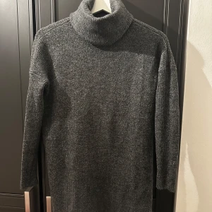 Grå stickad klänning - Mysig grå stickad klänning med polokrage, perfekt för kyliga dagar. Den har en hög polokrage och långa ärmar, vilket gör den superbekväm och varm. Passar perfekt till både vardag och lite finare tillfällen. Ett måste i garderoben för höst och vinter!