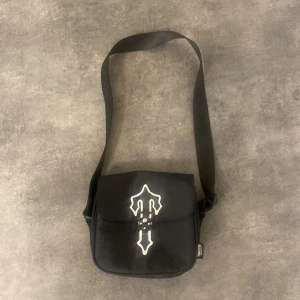 Svart axelväska med dekorativt mönster - Snygg svart axelväska med ett unikt vitt dekorativt mönster på framsidan. Väskan har en justerbar axelrem och en praktisk storlek för vardagsbruk. Perfekt för att bära med sig det nödvändigaste.