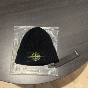 Stone Island mössa -  Aldrig använd Snygg svart ribbad mössa från Stone Island med det ikoniska broderade märket framtill. Perfekt för att hålla värmen med stil. Kommer i originalförpackning.