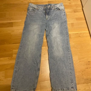 Blå jeansbyxor från H&M - Säljer ett par klassiska blå jeansbyxor från H&M med en avslappnad passform. Byxorna har en rak och bred stil med fem fickor och knappgylf. Perfekta för en casual look.
