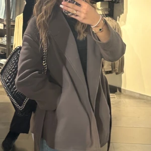 Brun kappa - Snygg brun kappa med en stilren design. Perfekt för höst och vår. Den har en klassisk passform och långa ärmar, vilket gör den både bekväm och elegant.