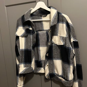Rutig overshirt i blått och vitt - Snygg rutig overshirt i blått och vitt med knappar framtill. Den har långa ärmar och två bröstfickor med lock. Croppad design.
