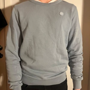Ljusblå tröja från Knowledge Cotton Apparel - Säljer en stilren ljusblå tröja från Knowledge Cotton Apparel i storlek S. Tröjan är i bra skick och har en liten logga på bröstet. Perfekt för både vår och höst, med långa ärmar och en bekväm passform. Passar till både vardag och avslappnade tillfällen.