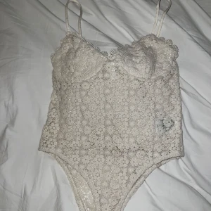 Beige spetsbody från H&M - Säljer en super fin beige spetsbody från H&M med tunna axelband och vacker blommig spetsdesign. 