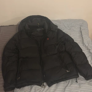 Svart dunjacka från Polo Ralph Lauren - Säljer en svart dunjacka från Polo Ralph Lauren med huva och dragkedja. . Perfekt för kyliga dagar. Använd knappt en vinter och är i toppskick. Köpt vid Zalando.