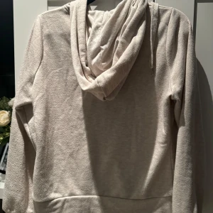 Beige hoodie med dragkedja - Mysig beige hoodie i mycket bra skick. Den har en praktisk dragkedja framtill och en stor huva med snören. Perfekt för kyliga dagar eller som ett extra lager under jackan. Den har också två fickor framtill för att värma händerna eller förvara småsaker.