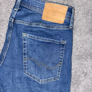 Blå jeans från Jack & Jones - Säljer ett par snygga blå jack&jones slim glenn jeans i bra skick. De har en klassisk femficksdesign och är perfekta för vardagsbruk. Jeansen har en slim passform och är tillverkade i slitstarkt denim