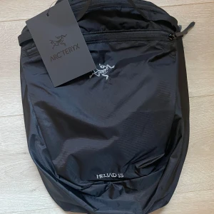 Svart ryggsäck från Arc'teryx - Snygg och praktisk svart ryggsäck från Arc'teryx, modell Heliad 15. Perfekt för vardagsbruk med en stilren design och slitstarkt material. Ryggsäcken har en dragkedja och justerbara remmar för bästa komfort.