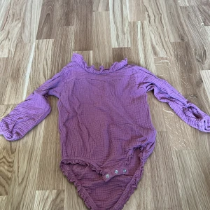 Lila body från So Cute - Säljer en söt lila body från So Cute med långa ärmar och knappar i grenen. Perfekt för små barn som vill ha något bekvämt och stiligt. 💜
