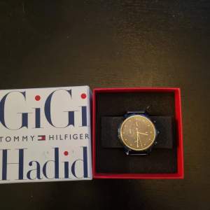 Säljer en stilren svart klocka från Tommy Hilfiger i samarbete med Gigi Hadid. Klockan har en elegant design med en marinblå urtavla och matchande armband. Perfekt för både vardag och fest. Kommer i originalförpackning. Nypris när den såldes va på 3000