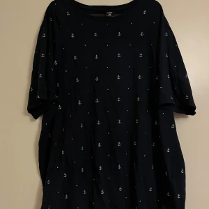Marinblå t-shirt med ankarmönster från new yorker - Säljer en snygg marinblå t-shirt från new yorker i storlek XXL. Den har ett coolt ankarmönster över hela tyget. Perfekt för en avslappnad stil eller en dag vid havet. T-shirten är kortärmad och gjord i ett bekvämt material.