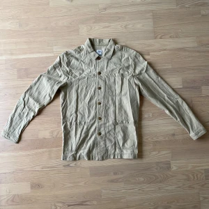 Beige overshirt från Zara - Säljer en snygg beige overshirt från Zara i storlek M. Den har en avslappnad stil med knappar framtill och tre praktiska fickor. Perfekt för vår och höst när du vill ha något lätt men ändå stiligt. Passar både till vardags och lite mer uppklädda tillfällen. Skick: Mycket bra - Artnr: B032