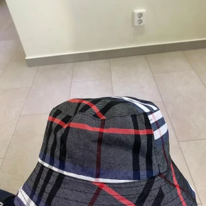 Rutig och svart bucket hat från Burberry - Säljer en snygg bucket hat från Burberry. Den är vändbar med en sida i klassiskt rutigt mönster i svart, rött och vitt, och den andra sidan är helt svart med diskret Burberry-logga. Perfekt för både sommar och höst! 🖤