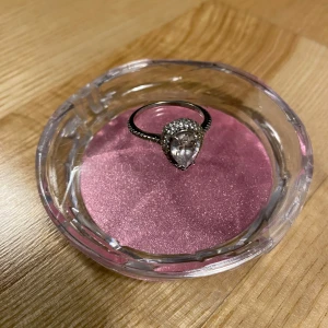 Silverring med stor glittrande sten - Säljer en elegant silverring med en stor, glittrande sten i droppform. Ringen har små stenar längs bandet som ger extra bling. Perfekt för speciella tillfällen eller som en statement piece i vardagen. Storleken är cirka 2 cm i diameter. Passar perfekt för dig som älskar att glänsa! 💍✨