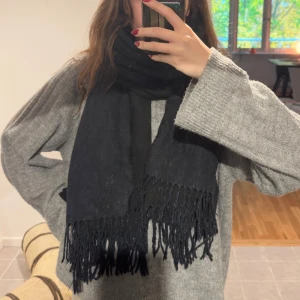 Svart halsduk med fransar - Säljer en snygg svart halsduk med fransar i ändarna. Den är perfekt för att hålla sig varm under kyliga dagar. Halsduken är mjuk och bekväm, vilket gör den idealisk för både vardag och fest. Passar perfekt till höst- och vinteroutfits!