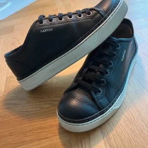 Lanvin Low Top sneakers DBB1 - Säljer ett par stilrena svarta sneakers från Lanvin i skinn. De har en klassisk design med snörning och en vit sula som ger en snygg kontrast. Perfekta för både vardag och festliga tillfällen. Skorna är i nyskick och redo för en ny ägare! Skick 8/10