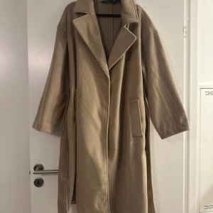 Kappa  - Lång kappa i storlek 42 i beige färg! Knyte med 2 fickor. Helt oanvänd men utan prislapp då jag var snabb att ta bort för trodde jag skulle använda men är lång på mig som är 160 cm. Passar även strl 40!