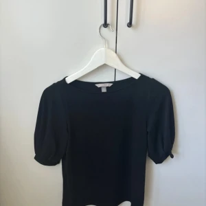 Svart kortärmad topp - Säljer en stilren svart topp med korta ärmar. Perfekt för både vardag och fest. Den har en enkel design som gör den lätt att matcha med olika outfits. Toppen är i bra skick och passar perfekt till både jeans och kjol.