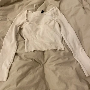 Vit ribbad topp - Säljer en superfin vit ribbad topp med långa ärmar. Den har en unik design med en fyrkantig halsringning och en liten cut-out detalj vid axeln. Perfekt för både vardag och fest!💕💕