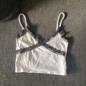 Vit linne med spetsdetaljer köpt från NewYorker - Säljer en söt vit linne från NewYorker i storlek XS. Den har tunna axelband och söta svarta spetsdetaljer längs kanterna och över bysten. Perfekt för sommardagar eller som ett lager under en tröja. Superfint skick! 