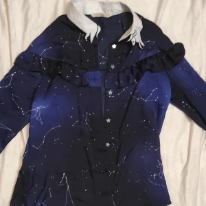 Mörkblå stjärnmönstrad Lolita inspirerad skjorta - Säljer en superfin mörkblå lolita skjorta med stjärnmönster och volangdetaljer. Den har långa ärmar och en unik krage med stjärnformade knappar. Perfekt för höst och vinter, eller varför inte till en fest med rymdtema? Skjortan är tunn och är i mycket bra skick och passar perfekt för dig som vill sticka ut!