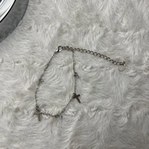 Silverfärgad fotlänk med kors - Snyggt och stilrent armband i silverfärg med små kors som detaljer. Perfekt för att ge en subtil men ändå personlig touch till din outfit. Justerbar kedja för att passa olika storlekar. Passar både till vardags och fest! Super fint skick då den aldrig blivit använd ☺️