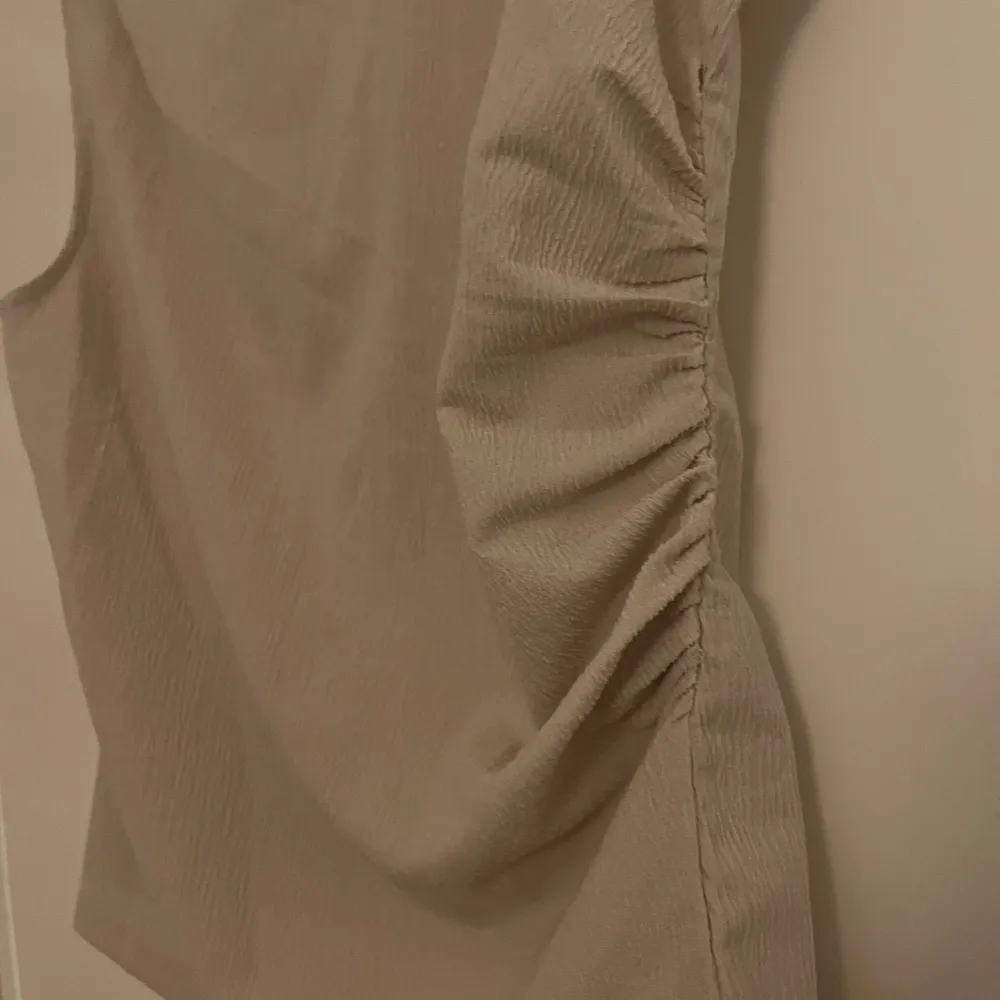 Säljer en stilren beige ärmlös topp från H&M i storlek M. Toppen har en elegant rynkad detalj på sidan som ger en fin passform. Perfekt för både vardag och festliga tillfällen. Materialet är mjukt och bekvämt. Aldrig använd! 💌. Yläosat.
