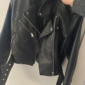 Svart skinnjacka från Pull&Bear - Säljer en snygg svart skinnjacka från Pull&Bear i storlek L men passar som S. Jackan har en cool bikerstil med dragkedjor och bälte i midjan. Perfekt för höst och vår, och den ger en edgy look till vilken outfit som helst. Använd ett fåtal gånger, så den är i mycket bra skick. Passa på att köpa denna stiliga jacka! 🖤