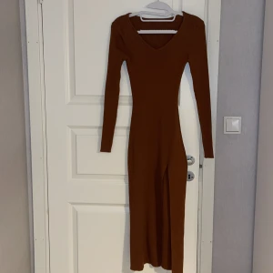 Brun långklänning med slits - Säljer en snygg brun långklänning i tight passform. Klänningen har långa ärmar och en stilren slits på sidan som ger en elegant touch. Perfekt för höst och vinter tillfällen. Passar både till vardags och festligare tillfällen. Endast använd en gång.