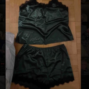 Mörk grönt satinpyjamas med spetsdetaljer - Säljer ett elegant mörk grönt satinpyjamas med vacker spetskant. Perfekt för en mysig hemmakväll eller som en del av en lyxig pyjamas. Linnet har en mjuk och glansig yta som känns skön mot huden.