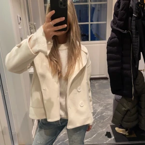 Vit kappa - Säljer en stilren vit kappa i mycket bra skick. Den har en klassisk design med stora knappar framtill och en snygg krage. Perfekt för höst och vår, och passar både till vardags och lite finare tillfällen. Jackan har långa ärmar och en normal passform. Superfin att matcha med jeans eller klänning!
