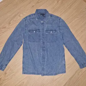 Säljer en snygg jeansskjorta från Tommy Hilfiger i storlek 164. Skjortan är i bra skick och har långa ärmar med knappar framtill. Perfekt för en avslappnad stil eller som en overshirt. Den har två bröstfickor med knappdetaljer och det klassiska Tommy Hilfiger-märket.