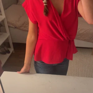 Röd omlottblus - Säljer en snygg röd omlottblus med korta ärmar. Perfekt för både vardag och fest! Blusen har en knytning i midjan och är ganska så trendig. Har aldrig kommit till användning bara provad💕❤️❤️❤️