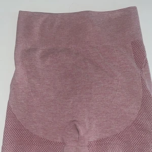 Rosa Träningsshorts  - Säljer ett par rosa Träningsshorts i mycket bra skick. De är högmidjade och har en tight passform som ger bra stöd under träningen. Materialet är mjukt och stretchigt, perfekt för gymmet eller yoga. Shortsen har en snygg design med mönstrade detaljer som ger extra stilpoäng.