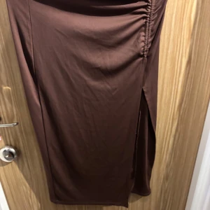 Brun kjol med slits - Snygg brun kjol i ett mjukt material med en elegant slits på sidan. Perfekt för både vardag och festliga tillfällen. Kjolen har en smickrande passform och är lätt att matcha med olika toppar och skor.