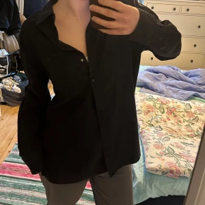 Svart skjorta - Säljer en stilren svart skjorta med långa ärmar i sammetsliknande finish. Lätt oversized look. 