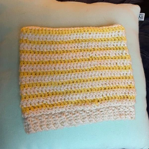 Randig virkad mössa i gult och vitt - Superfin virkad barn mössa med ränder i gult och vitt. Den har en söt design med små öron på toppen, perfekt för att hålla värmen under kyliga dagar. Passar bra för både höst och vinter. Mått, bredd: 23cm. Runt hela: 46cm.  !Obs! Mössan är inte så töjbar runt mudden! 🫶