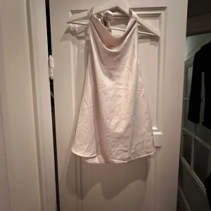 Vit/beige axelbandslös topp - Säljer en superfin satin vit/beige axelbandslös topp med knytning i nacken. Perfekt för alla fester! Den är i mycket bra skick och redo för nya äventyr. Skrynklig pga legat i påse på vinden🤍