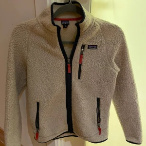 Beige fleecejacka från Patagonia - Säljer nu min kärade Patagonia fleece. Den har varit med länge nu och jag har tyvärr växt ut den. Den har några skavanker då det har försvunnit lite ull på underarmarna. Annars väldigt fin kvalitet. Patagonia är ju ett känt märke med bra kvalitet. Storleken är XL fast det är i barn storlek. Jag skulle säga att den passar någon i 14års åldern vid ungefär 152-158cm lång.                         Mvh Hugo!