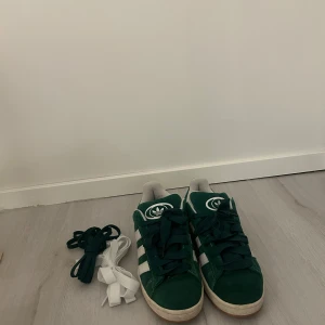 Gröna Adidas Campus sneakers - Säljer mina adidas campus 00. Skitsnygga och i riktigt bra skick. Köpte dem tidigare detta året men kommer knappt till användning då det inte riktigt går ihop med min stil känner jag. Hör av dig vid frågor!😊 Tillkommer också två extra snören som aldrig används (vita samt smalare gröna)