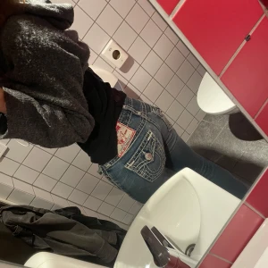 Blå jeans från True Religion - Säljer ett par snygga blå jeans från True Religion. De har en cool slitning och detaljerade bakfickor med knappar.