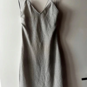Glittrig silverklänning från H&M - Säljer en superfin glittrig silverklänning från H&M i storlek XXS. Klänningen har en v-ringad design med tunna axelband och en öppen rygg som ger en elegant look. Perfekt för festliga tillfällen! ✨