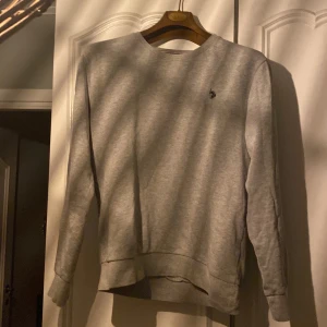 Grå sweatshirt från U.S. Polo Assn. Storlek M  - Säljer en stilren grå sweatshirt från U.S. Polo Assn. i mycket bra skick. Tröjan har en liten broderad logga på bröstet och är perfekt för både vardag och avslappnade tillfällen. Den är gjord i mjukt material och har långa ärmar.