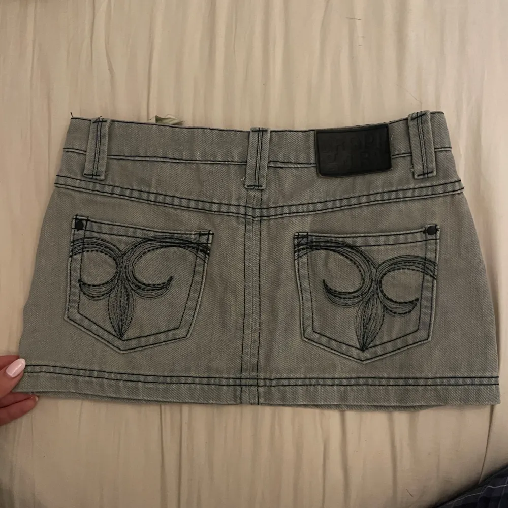 Säljer en supercool lågmidjad jeanskjol från Crop Girl. Den har snygga broderade detaljer på bakfickorna som gör den unik. Perfekt för en avslappnad look eller en utekväll. Passar perfekt till vår och sommar! Kjolen är i toppen skick utan några somhelst defekter!🩷🩷. Kjolar.