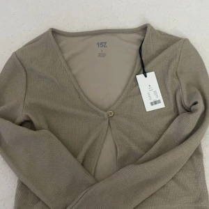 Beige ribbad kofta från 157 - Säljer en superfin beige kofta från 157 i storlek S. Den är ribbad och har en enkel knapp framtill. Perfekt för höst och vår med sina långa ärmar och mjuka material. Ny med tag kvar!