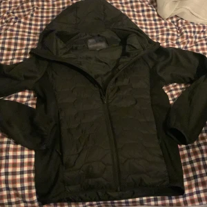 Svart cardigan men väst detaljer  - Säljer en svart cardigan jacka i mycket bra skick. Den har en praktisk huva och dragkedja framtill. Perfekt för höst och vår när det är lite kyligare ute. Jackan är stilren och passar till det mesta. Hör av dig om du är intresserad!