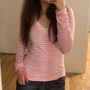 Rosa och vit randig tröja - Säljer en superfin rosa och vit randig tröja med v-ringning. Den är långärmad och har en tight passform som sitter snyggt på kroppen. Står storlek M på den men tycker den passar bra som S/Xs oxå💗
