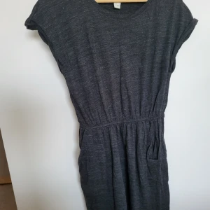 Klänning  - En grå klänning med korta ärmar och en ficka på sidan. Den har en elastisk midja och är gjord av ett mjukt och bekvämt material