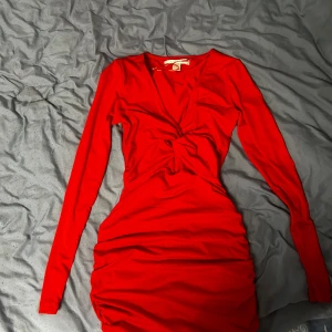 Röd långärmad klänning med knytning - Säljer en superfin röd klänning med långärmade och en snygg knytning framtill. Perfekt för festliga tillfällen! Klänningen har en tight passform som framhäver figuren och är gjord i ett mjukt och stretchigt material. Aldrig använt.